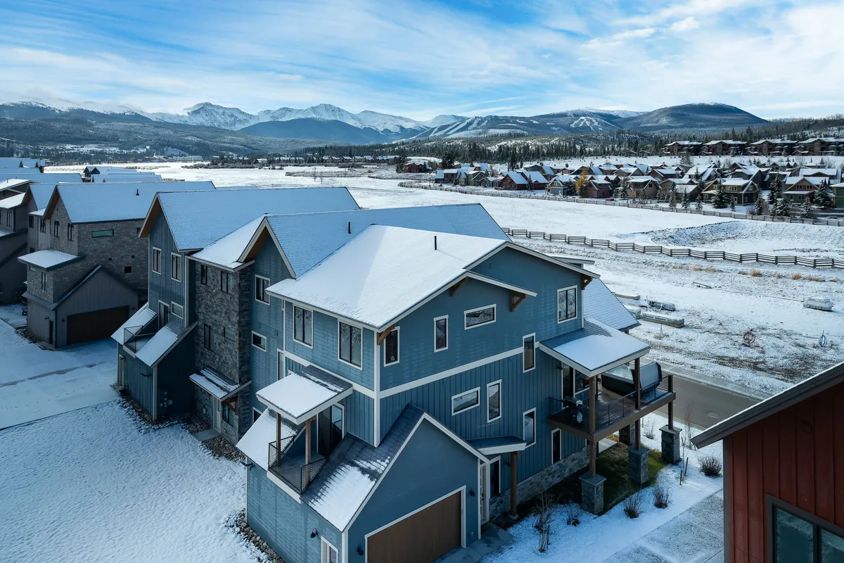 A snow-covered house set against a dramatic mountain backdrop, surrounded by a spacious landscape. The scene captures the essence of winter, with untouched snow blanketing the ground and the peaks rising in the distance, inviting thoughts of skiing, snowboarding, and cozy evenings inside.