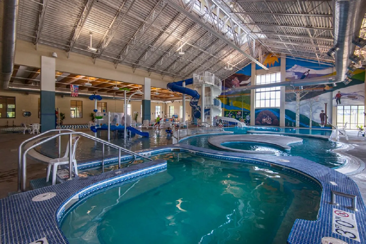A joyful interior image of the Grand Park Rec Center’s pool area, featuring children playing on water slides, a sparkling swimming pool, and a bright mural, all radiating energy and fun.