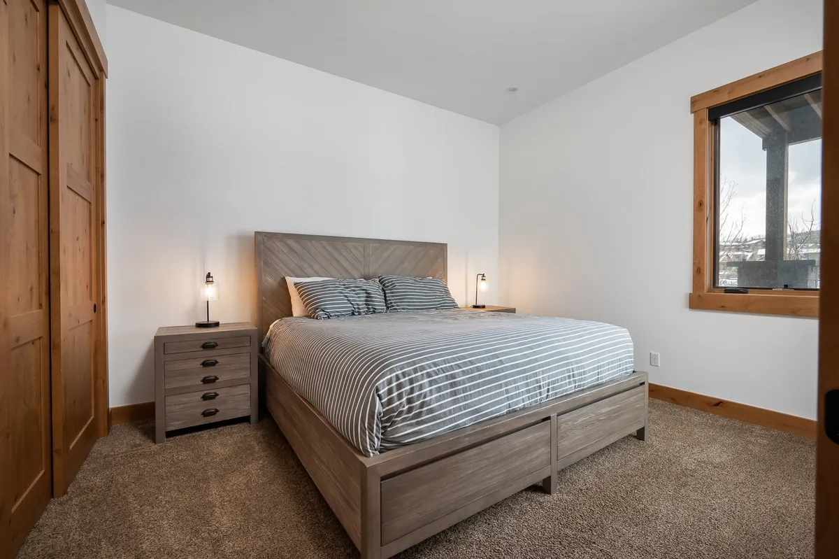 A tranquil bedroom scene featuring a bed with striped bedding, nightstands on each side with lamps, and a window letting in soft natural light. The room exudes an inviting and restful atmosphere, perfect for unwinding after a long day.