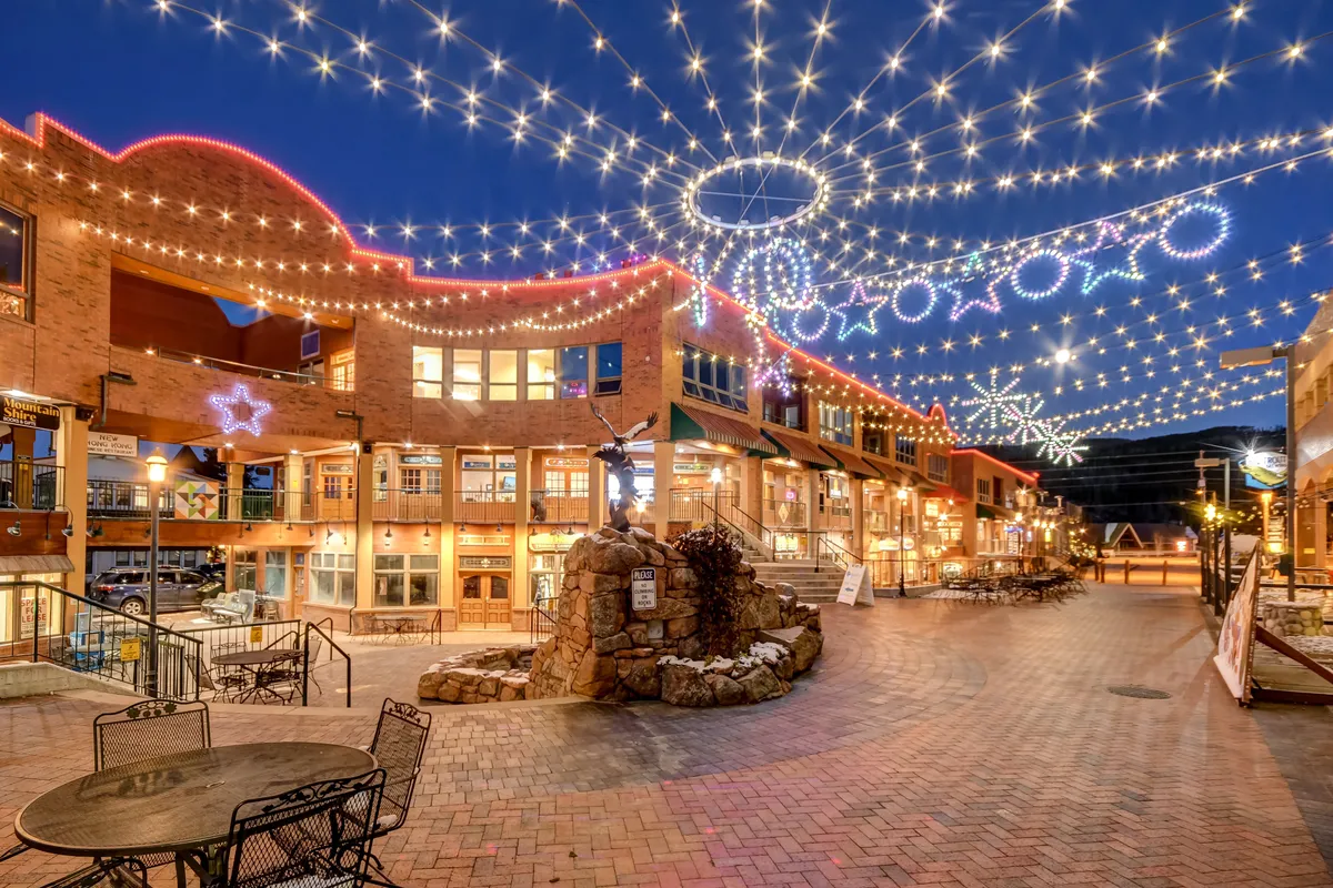 A lively, pedestrian-friendly street scene featuring string lights, decorative stars, cobblestone paths, outdoor seating, and charming storefronts. The image evokes a sense of community, celebration, and year-round vibrancy, hinting at festivals, markets, and events.
